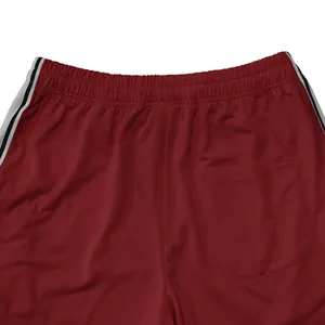 Detail van rode sportbroek met een elastische tailleband, achterzak en de zijstrepen.