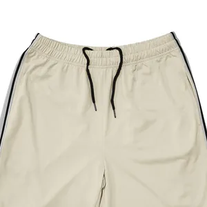 Detail van een beige sportbroek met elastische taille en zwart trekkoordje accent.