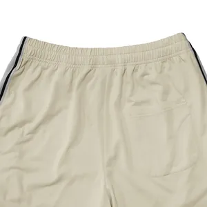 Detail van elastische tailleband en achterzak op beige sportbroek met zijstrepen.