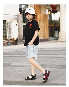 Young boy wearing black velcro sandals and denim shorts walking on an outdoor sidewalk
