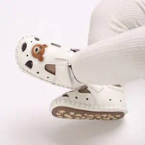 Detalle de sandalias blancas de bebé con oso de dibujos y suela antideslizante