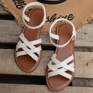 Detailansicht der weißen Riemchensandalen auf einer Holzoberfläche mit Strohhut.