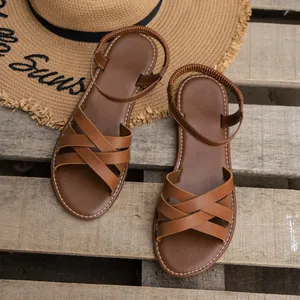 Braune flache Riemchensandalen für Damen auf einer Holzpalette mit einem Strohhut