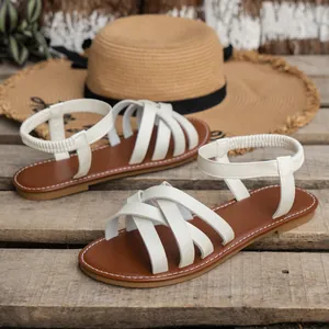 Detailansicht der weißen flachen Sandalen mit Kreuzgurten auf rustikalem Holz.