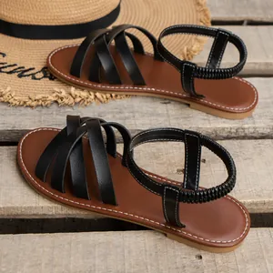 Detailansicht von schwarzen Damen Riemchensandalen auf Holzoberfläche mit einem Strohhut.