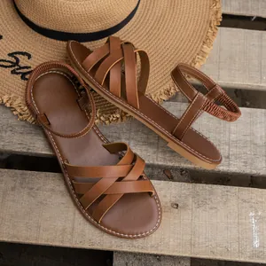 Detailansicht brauner flacher Sandalen mit Kreuzriemen auf einem Holzhintergrund