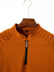 Gros plan sur l'épaule plissée et le col zippé d'un polo orange à manches longues.