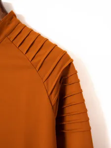 Close-up detail of pleated shoulder design on a burnt orange men's long sleeve polo shirt