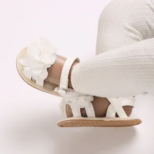 Primer plano de sandalias blancas para bebé con grandes flores 3D y suelas planas.