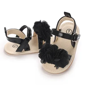 Detalle de sandalias para bebé con correas de charol negro y grandes flores de tela