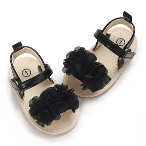 Primer plano de sandalias para bebé niña con elegante flor de tela negra y charol brillante.