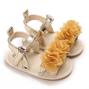 Primer plano de sandalias doradas para bebé niña con flores decorativas de tela amarilla.