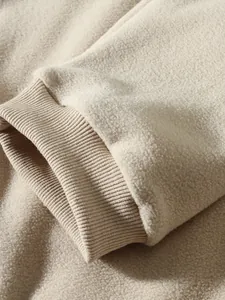Nahaufnahme der weichen Fleece-Textur und der gerippten Manschette eines beigen Sweatshirts.