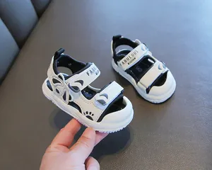 Primo piano di sandali per bambini bianchi e neri con chiusura a strappo e punta chiusa.