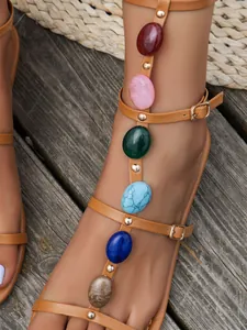 Close-up of tan gladiator sandals with colorful stones and gold studs decoration