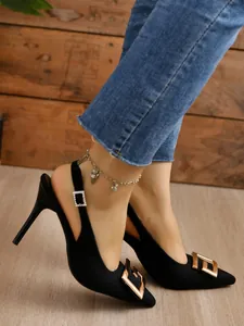 Detail of black pointed-toe slingback heels with large gold buckle and slim stiletto