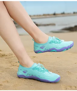 Muntgroene waterschoenen met paarse zolen gedragen op een zandstrand setting