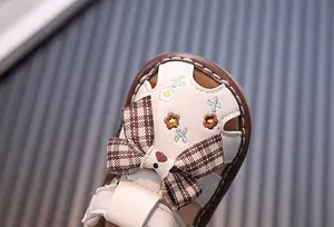 Detaillierte Nahaufnahme von Baby-Sandalen mit karierter Schleife und Blumenstickerei