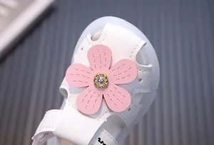 Nahaufnahme einer weißen Babysandale für Mädchen mit rosa Blume und Schmuckstein