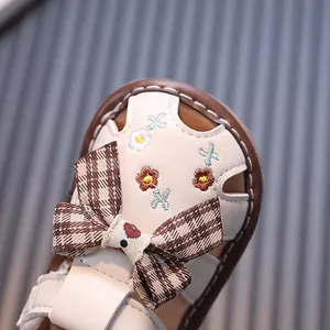 Nahaufnahme von niedlichen Babysandalen für Mädchen mit Karoschleife und Blumenstickerei