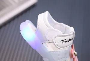 Detail einer weißen Babysandale mit blauer LED-Leuchtsohle und Blumenakzent.