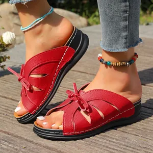 Nahaufnahme roter Damen-Keilsandalen mit dekorativer Schleife und weißen Ziernähten
