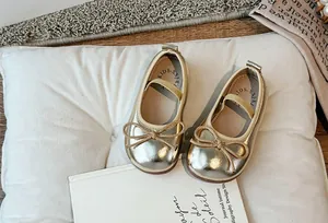 Dettaglio di eleganti ballerine dorate per bambina con un grazioso fiocco su cuscino bianco.