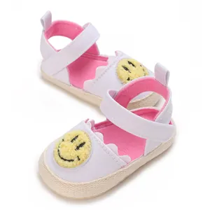 Dettaglio di scarpe primi passi per neonati con patch smiley giallo e fodera rosa.