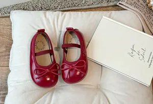 Scarpe di vernice rossa per bambina con fiocco su un cuscino bianco trapuntato