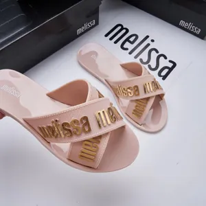 Detailed macro view of Melissa pink jelly slides with gold logo letters on cross straps