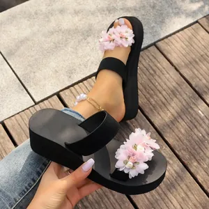 Close-up of stylish black platform sandals with pink floral decoration for beach wear.