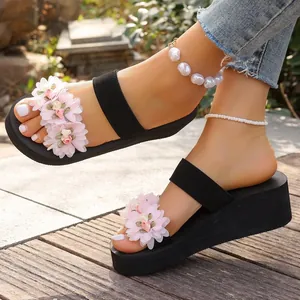 Close-up of black platform wedge sandals with pink floral decorations on a wooden deck