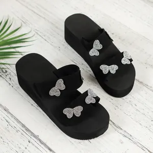Detail view of stylish black platform wedge slippers with rhinestone butterfly accents