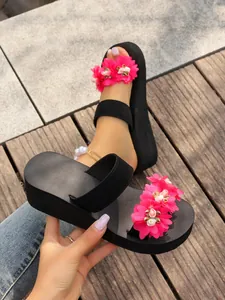 Close-up detail of women's black wedge slippers with pink floral embellishments