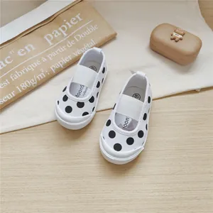 Detail view of white canvas shoes with black polka dots and elastic strap for girls