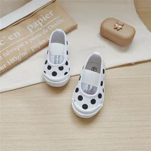 Detail shot of toddler girls' white canvas shoes with black polka dots and elastic strap.