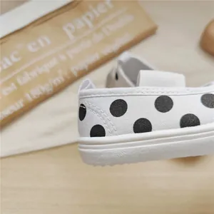 Close-up of white canvas toddler shoes with black polka dots and soft white sole