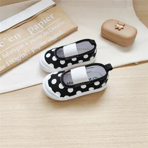 Close-up of black polka dot toddler canvas shoes with soft soles on wood surface.