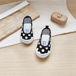 Toddler black and white polka dot canvas shoes with soft soles on a wooden background.