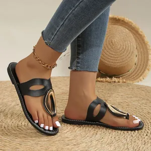 Close-up of black flat sandals with gold metal buckle on a woven straw mat