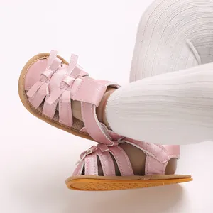 Detalle de sandalias rosas brillantes para bebé con lazo y suela de goma marrón