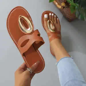 Detail of tan flat sandals featuring a large oval gold metal buckle on the T-strap.