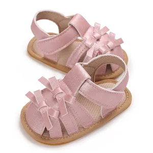 Detalle de sandalias de bebé en rosa brillante con lazos y suelas blandas antideslizantes.