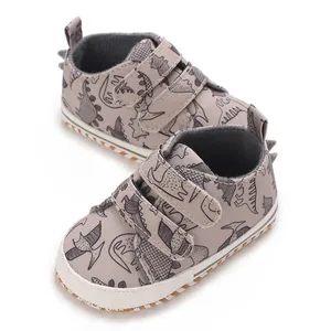 Detailed view of baby boy's grey dinosaur print sneakers with double velcro straps.