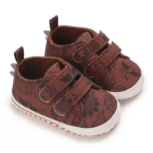 Detailed close-up of brown infant sneakers with black dinosaur prints and velcro.