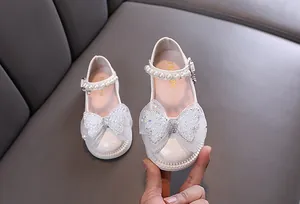 Nahaufnahme weißer Prinzessinnenschuhe für Mädchen mit glitzernder Schleife und Perlenriemen