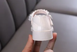 Nahaufnahme eines weißen Mädchen-Prinzessin-Schuhs mit Perlenriemen und Strass-Detail