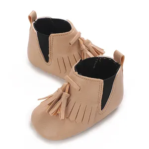 Nahaufnahme von beigen Baby-Boots mit stilvollen Fransen und weichen Stoffsohlen für Kleinkinder