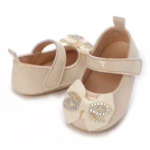 Detail view of beige baby girl walker shoes featuring a large rhinestone bow and soft sole