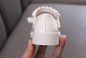 Nahaufnahme der cremefarbenen Lackleder-Mädchenschuhferse mit elegantem Perlenriemen